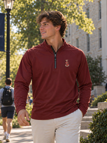 College-aged man wearing a maroon Cutter + Buck Adapt quarter zip with embroidered chest crest and khaki pants while walking outdoors on a college campus.