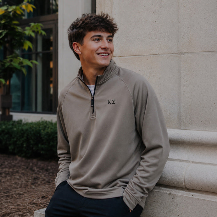 College-aged man wearing the Mushroom Cutter & Buck Adapt quarter-zip with black embroidered Kappa Sigma Greek letters outdoors on campus.