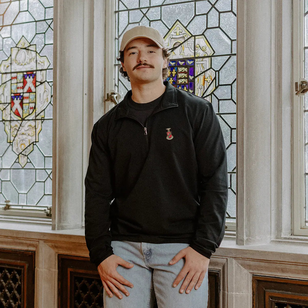 Male model wearing the black Kappa Sigma Embroidered Luxe Quarter Zip in front of stained glass windows with fraternity crests.