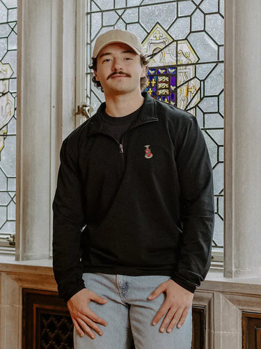 Male model wearing the black Kappa Sigma Embroidered Luxe Quarter Zip in front of stained glass windows with fraternity crests.