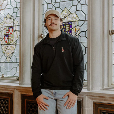 Male model wearing the black Kappa Sigma Embroidered Luxe Quarter Zip in front of stained glass windows with fraternity crests.
