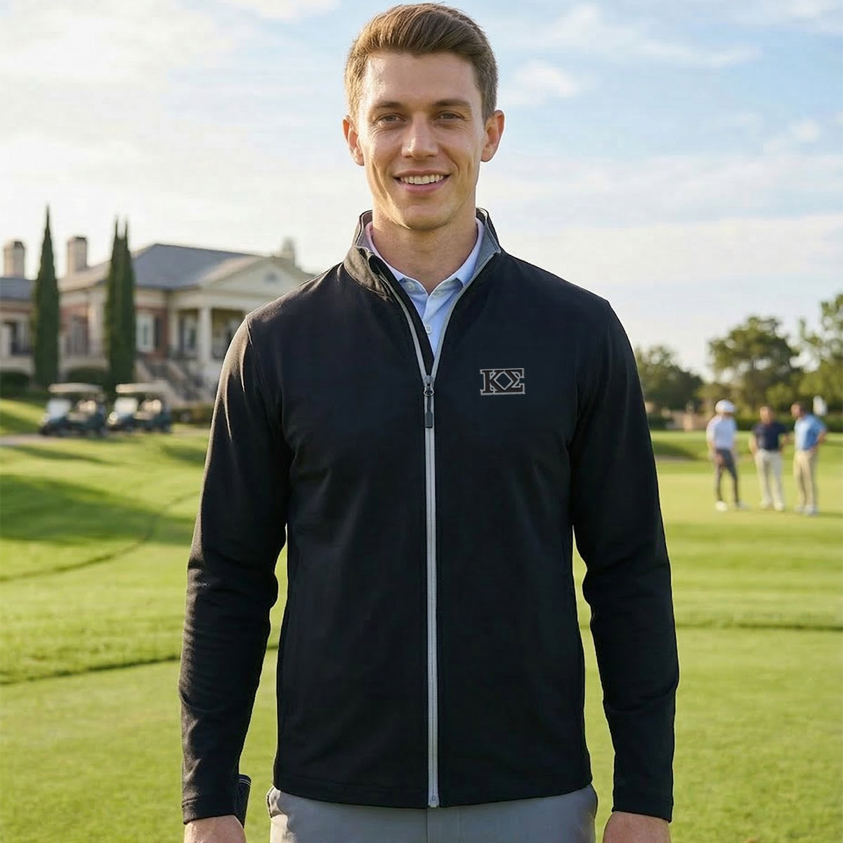 Fraternity wearing a black Callaway water-repellent golf jacket standing on a golf course in front of a clubhouse