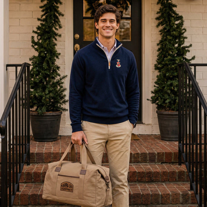 College student wearing fraternity quarterzip holding a tan canvas duffle bag with a leather patch.